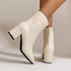 Side profile of beige ankle boot with pointed toe and block heel, styled on model's leg