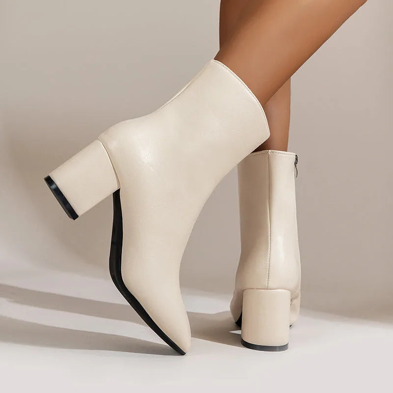 Side profile of beige ankle boot with pointed toe and block heel, styled on model's leg