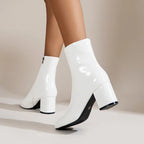 Side view of white patent ankle boots on model with one foot lifted, showing block heel