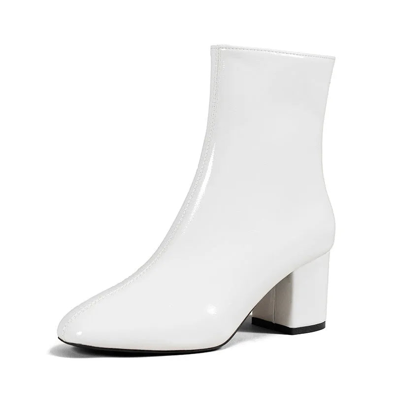 Side profile of glossy white ankle boots on model, showing zip fastening and heel shape