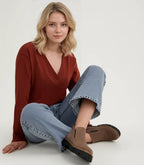 Model seated wearing taupe suede ankle boots with wide-leg denim jeans and a rust jumper