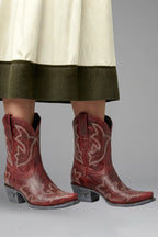 Close-up of red embroidered ankle boots peeking out from beneath an ivory and olive midi skirt