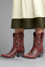 Front view of red leather ankle boots with embroidered shaft worn beneath a flowing skirt hem