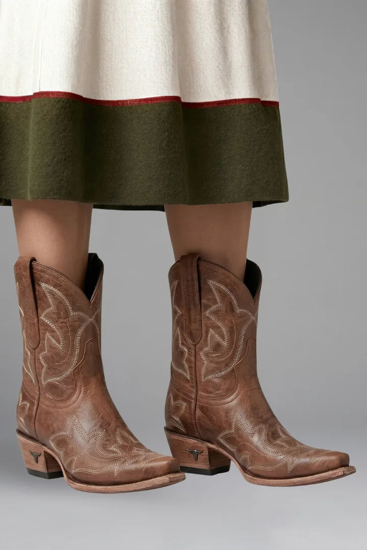Brown leather ankle boots with cream embroidered stitching worn beneath a green and cream skirt