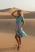 Side profile of the flowing floral midi dress caught in the wind against sand dunes.