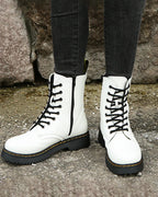 White lace-up ankle boots with side zip and black laces, shown against a stone wall backdrop
