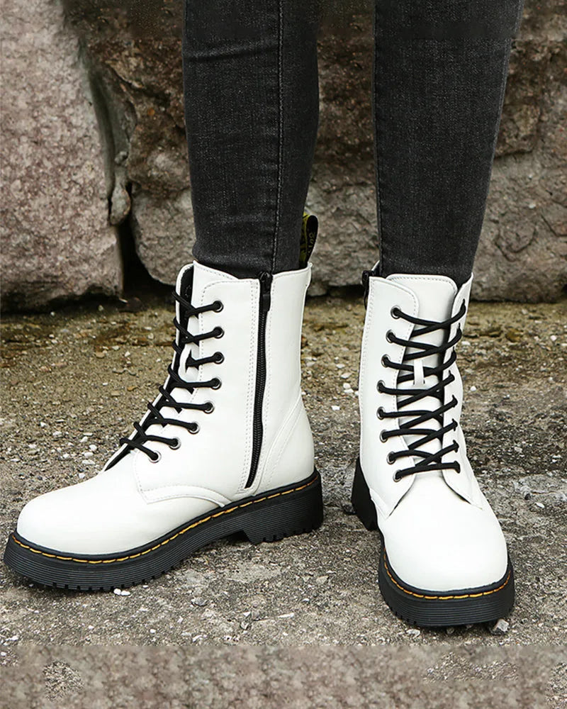 White lace-up ankle boots with side zip and black laces, shown against a stone wall backdrop