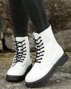 Front view of white lace-up boots on textured pavement, showing round toe shape and contrast stitching