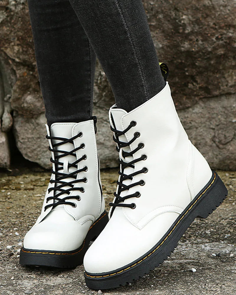 Front view of white lace-up boots on textured pavement, showing round toe shape and contrast stitching