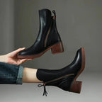 Side view of black leather ankle boot held by hand, showing block heel and vertical zip detail