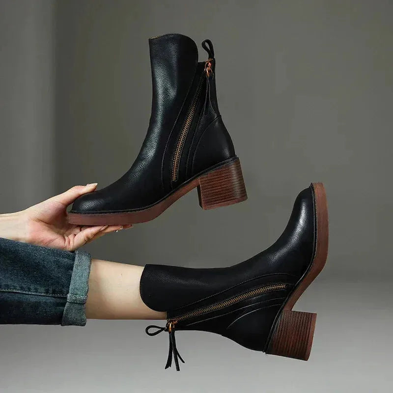 Side view of black leather ankle boot held by hand, showing block heel and vertical zip detail