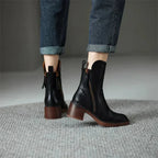 Rear view of black leather ankle boots on model's feet, showing stacked block heel and back loop tab
