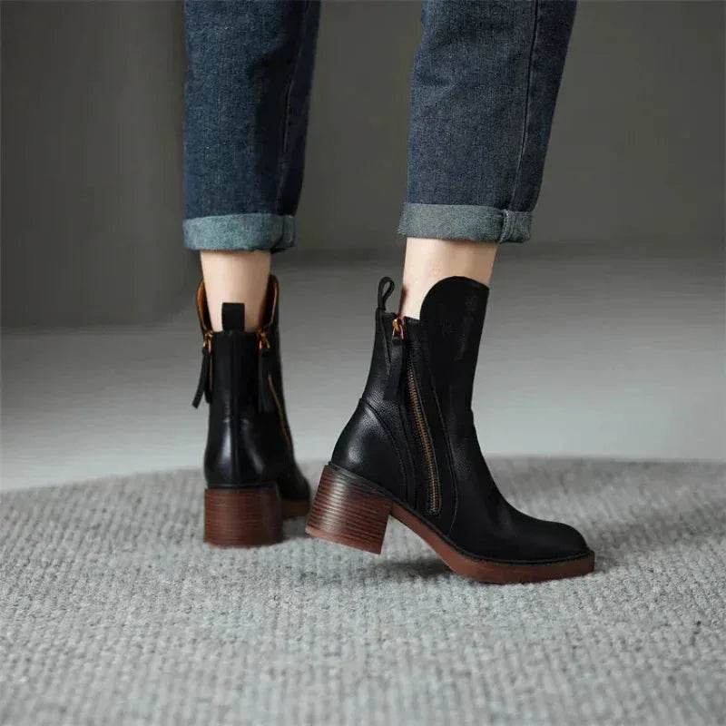 Rear view of black leather ankle boots on model's feet, showing stacked block heel and back loop tab