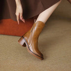 Side profile of brown leather ankle boot on model's foot, worn with a brown skirt, showing rounded toe