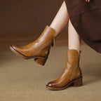 Front angled view of two brown leather ankle boots on model, highlighting zip trim and stacked heel