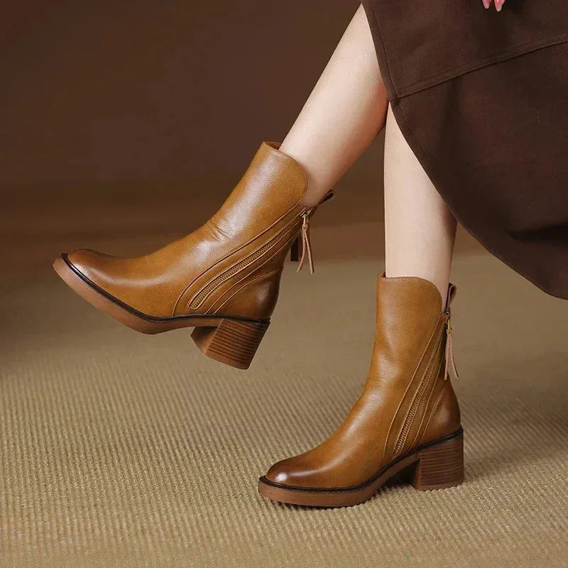 Front angled view of two brown leather ankle boots on model, highlighting zip trim and stacked heel