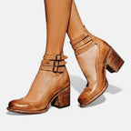 Side view of light brown leather ankle boots with triple ankle straps, block heel and rounded toe, worn on bare legs