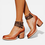 Close-up of brown leather ankle boots showing dark triple buckle straps, block heel and back zip closure