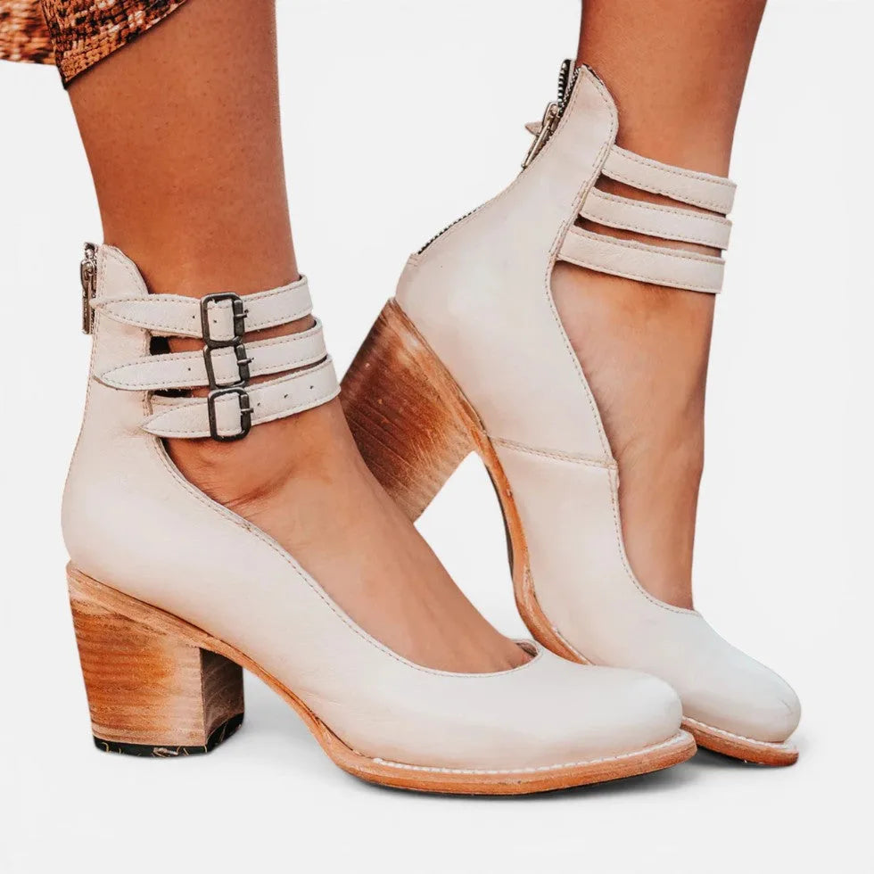 White leather ankle boots with three buckle straps and a stacked block heel, shown from the side on bare feet