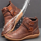 Brown leather ankle boots with side lacing and buckle strap detail, shown against a splash of water