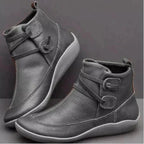 Grey leather ankle boots with buckle strap and contrast white stitching on a flat sole