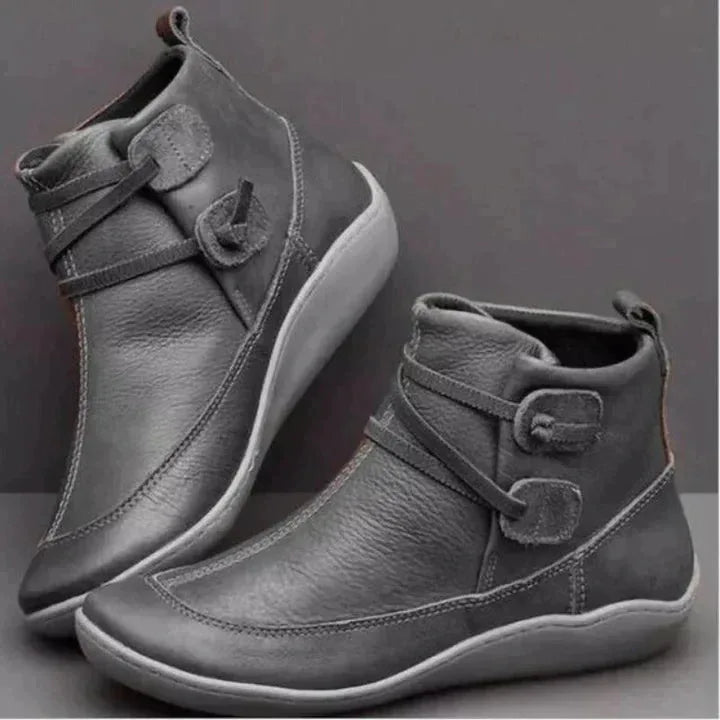 Grey leather ankle boots with buckle strap and contrast white stitching on a flat sole