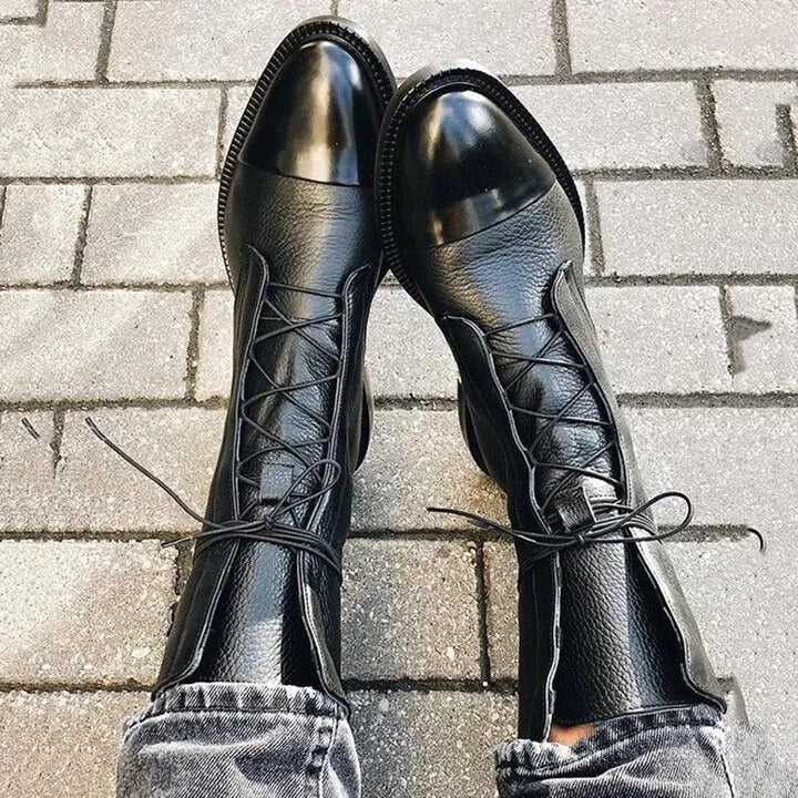 Top-down view of black lace-up boots showing crossed laces and glossy cap toe detail against paving stones