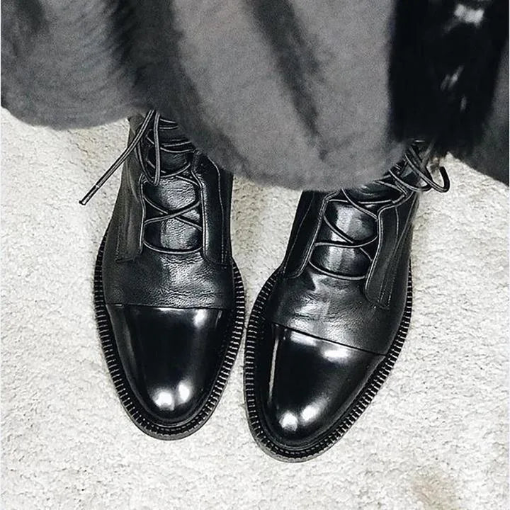 Close-up of black leather boot fronts with polished toe cap and criss-cross lacing on a light rug
