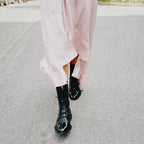 Side profile of black lace-up boots worn with a flowing pink midi dress, seen from behind while walking