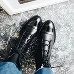 Black ankle boots with shiny cap toe worn with a blush pink dress, standing on a paved street