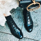 Overhead shot of black lace-up boots with visible stitched sole detail, worn with distressed denim on a patterned rug