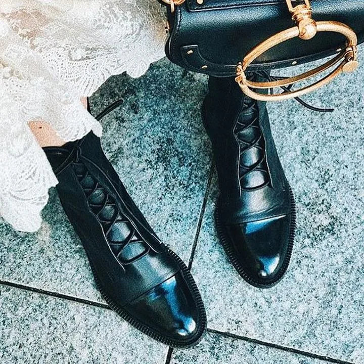 Overhead shot of black lace-up boots with visible stitched sole detail, worn with distressed denim on a patterned rug