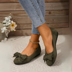 Side view of dark green bow ballet flats worn with cropped jeans and a gold chain anklet