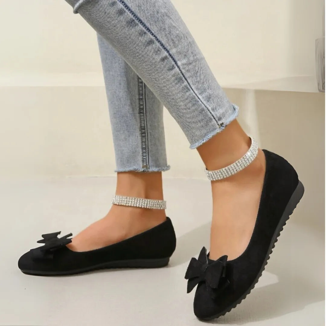 Side view of black bow ballet flats worn with a diamante ankle strap and cropped jeans
