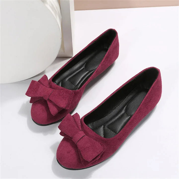 Angled top view of a pair of bordeaux bow ballet flats with black outsole placed on a white surface