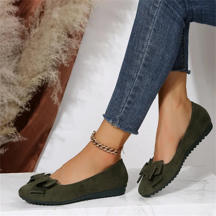 Side view of dark green bow ballet flats worn with cropped jeans and a chunky gold anklet