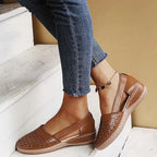 Brown leather flat with cut-out ankle design and tan wedge sole, worn on a wooden step
