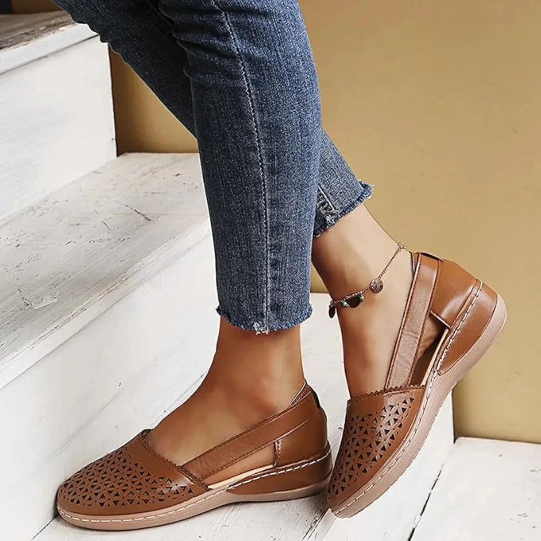 Brown leather flat with cut-out ankle design and tan wedge sole, worn on a wooden step