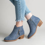 Side view of blue faux-suede ankle boot worn with cropped jeans, showing gold-tone side zip and stacked block heel