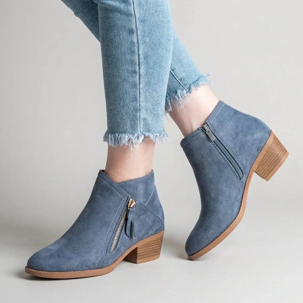 Side view of blue faux-suede ankle boot worn with cropped jeans, showing gold-tone side zip and stacked block heel