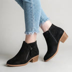 Black faux-suede ankle boot with topstitched seam and side zip, styled with raw-hem denim, stacked heel visible