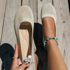 Beige knit ballet flats with tan cushioned insole, one held in hand and one worn on foot