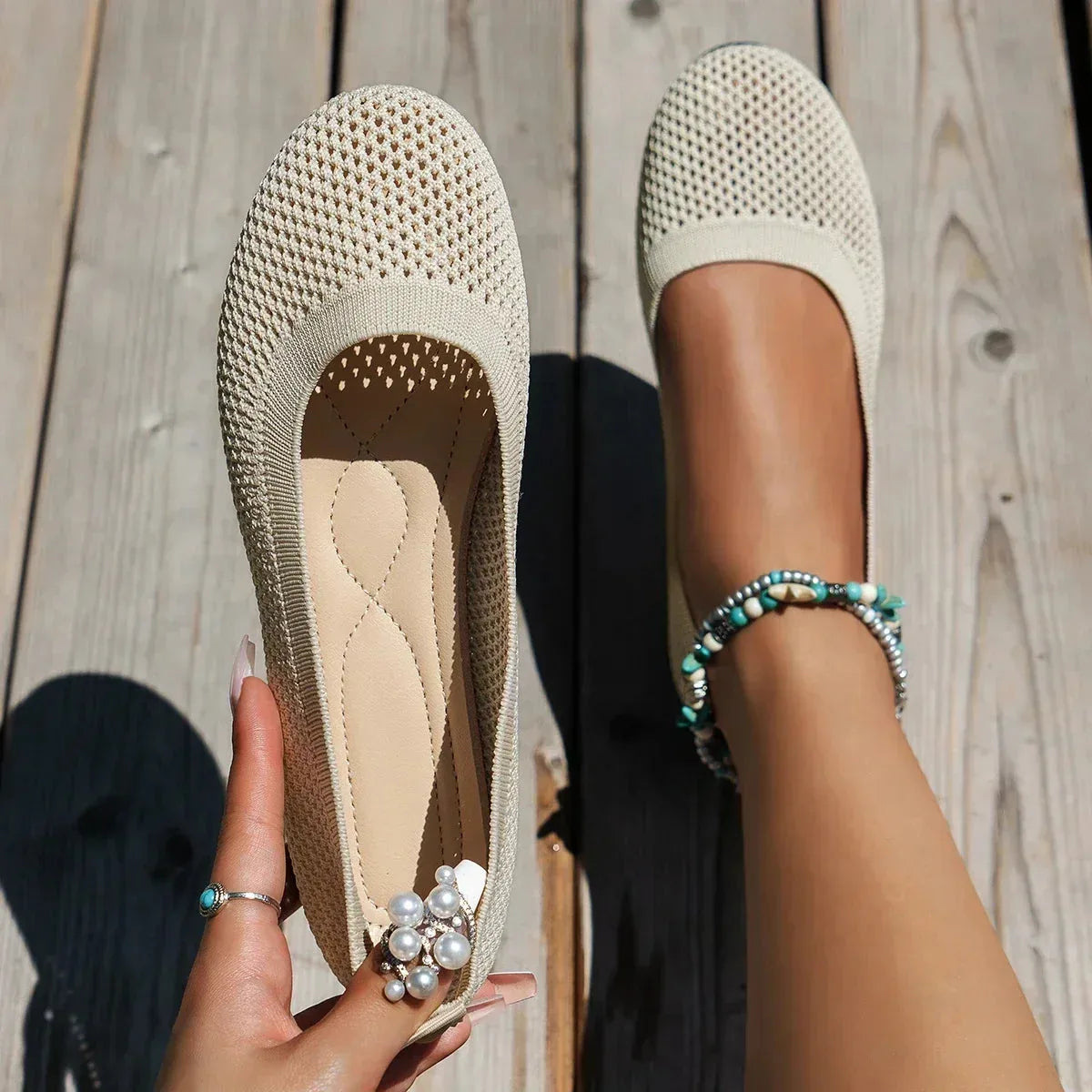 Beige knit ballet flats with tan cushioned insole, one held in hand and one worn on foot