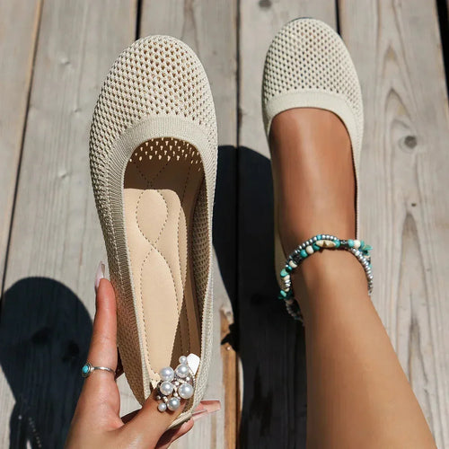 Beige knit ballet flats with tan cushioned insole, one held in hand and one worn on foot