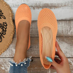 Orange mesh ballet flats resting on wooden boards, one shoe held to show interior cushioning