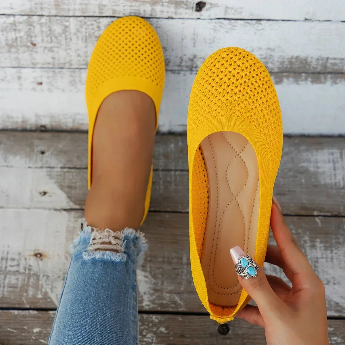Yellow knit ballet flats shown together, one worn on foot beside a woven straw mat