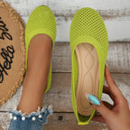 Green mesh ballet flats with tan insole, one held in hand and one worn on foot outdoors