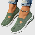 Green knitted slip-on trainer with side cut-out, worn on foot with rolled denim and beaded anklet