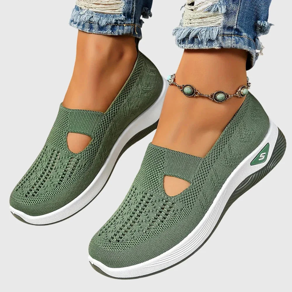Green knitted slip-on trainer with side cut-out, worn on foot with rolled denim and beaded anklet