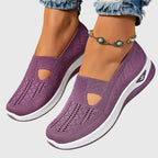 Purple knitted slip-on trainers shown from above resting in hand, revealing perforated sole